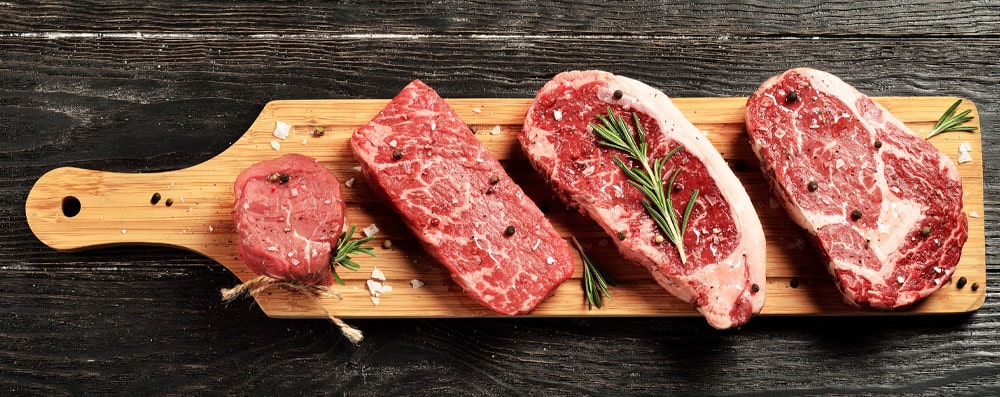 Image of several steaks marinating on a cutting board